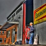 elderly man leaning against old metal building - Brown's Feed Store