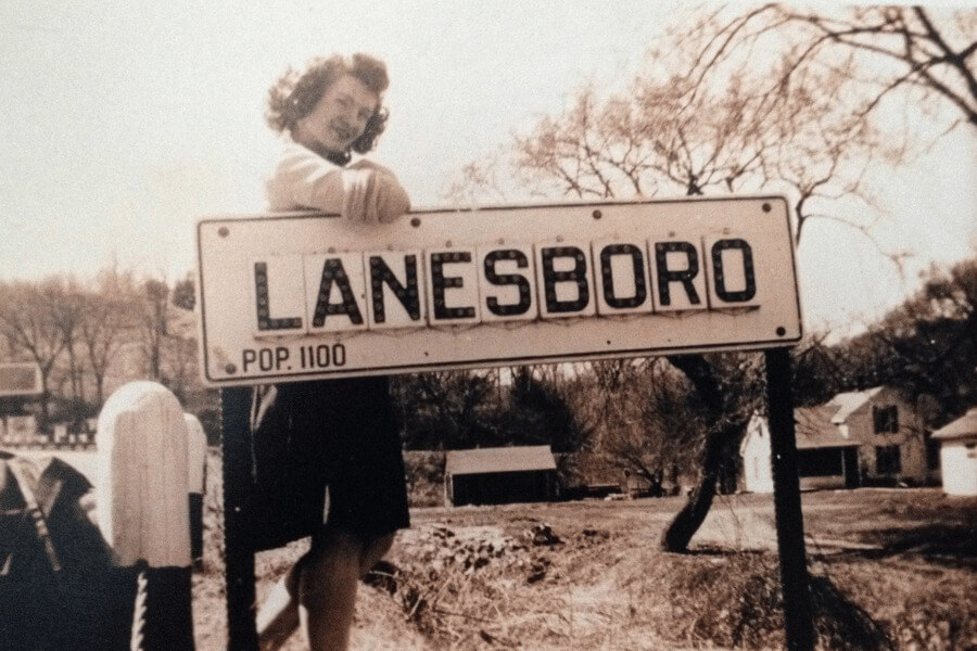 A woman standing by a sign that says "Lanesboro Pop. 1100"