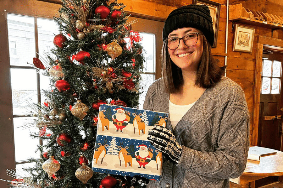 A woman smiling next to a Christmas tree at Stone Mill Clothing & Gifts in Lanesboro, MN