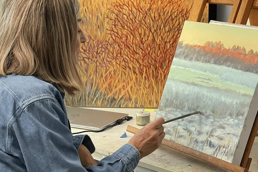 A woman painting a landscape scene in a studio