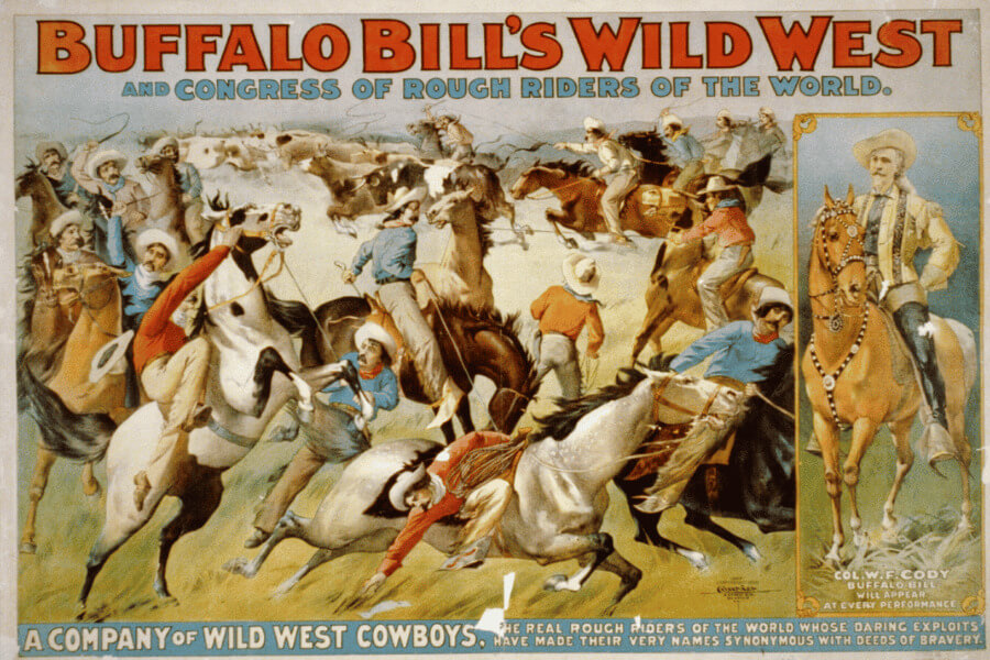 Colorful vintage poster advertising “Buffalo Bill’s Wild West and Congress of Rough Riders of the World.” The image shows a dramatic scene of cowboys on horseback engaged in action-packed stunts, riding, and roping. On the right side is a portrait of Buffalo Bill (Col. W.F. Cody) on a horse, dressed in buckskins and holding a rifle. Text along the bottom reads: “A Company of Wild West Cowboys. The real rough riders of the world whose daring exploits have made their very names synonymous with deeds of bravery.”