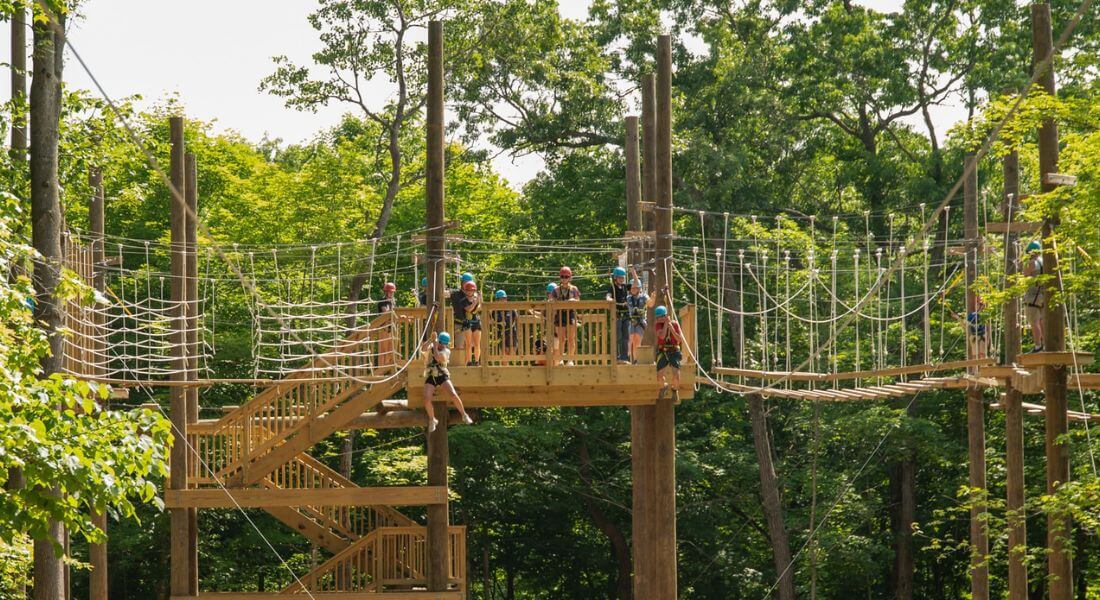 Participants wearing helmets and harnesses navigate the elevated high ropes course at Eagle Bluff Environmental Learning Center, surrounded by lush green trees.