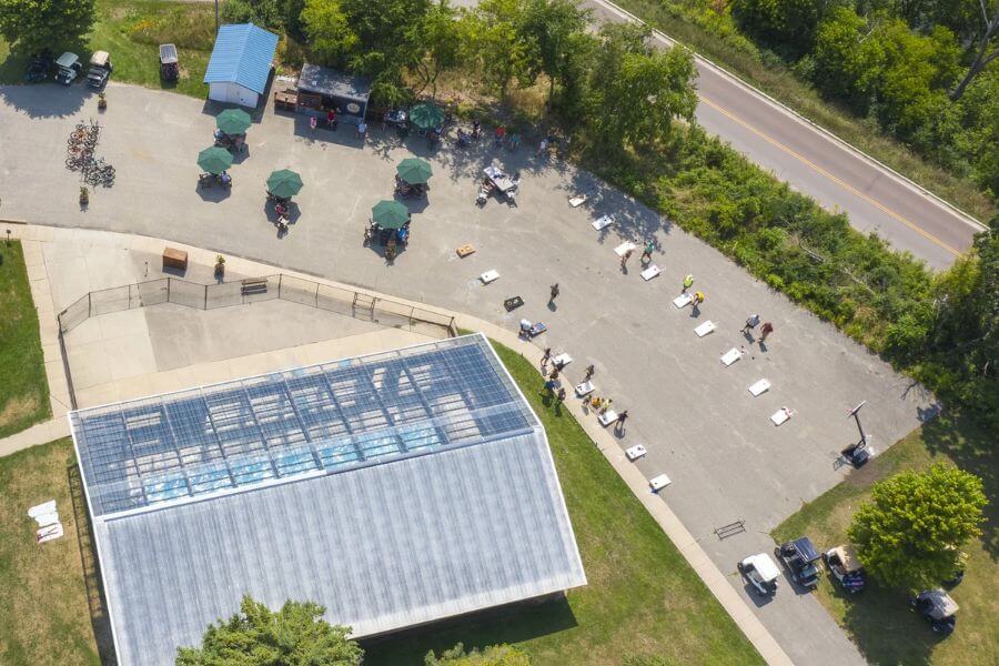 Aerial view of the Old Barn Resort’s activity area featuring “The Shed,” with its covered pool building, outdoor seating with umbrellas, and a row of cornhole boards set up for games.