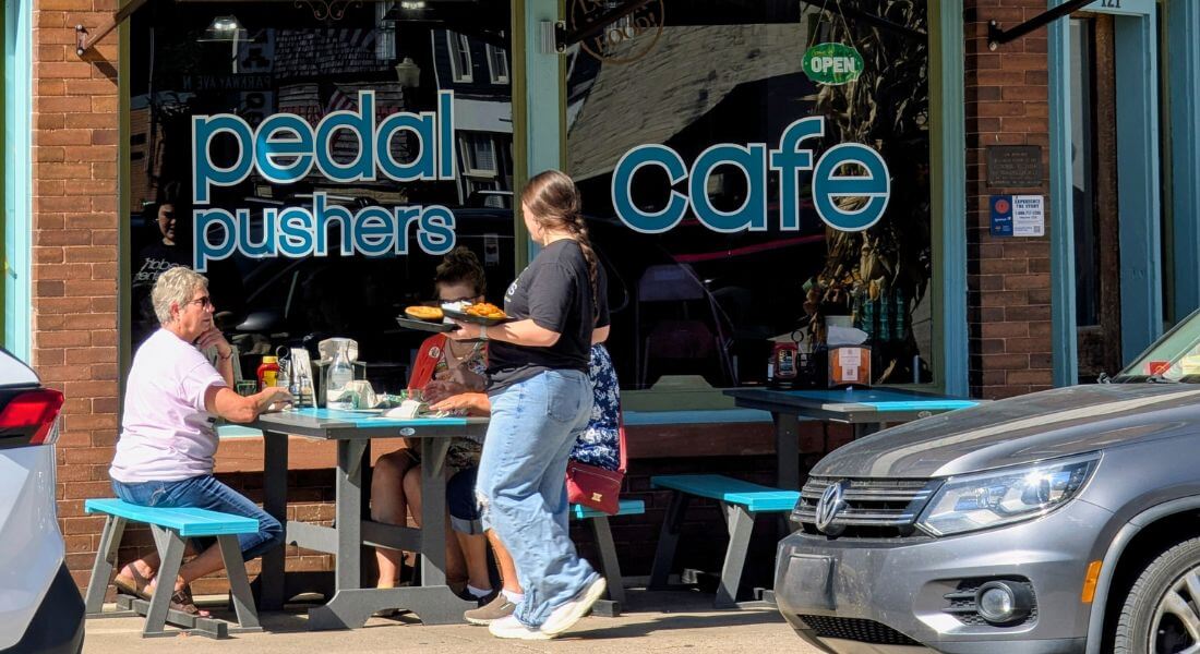 Server delivers plates of food to guests seated at outdoor picnic tables in front of Pedal Pushers Café in downtown Lanesboro, Minnesota.