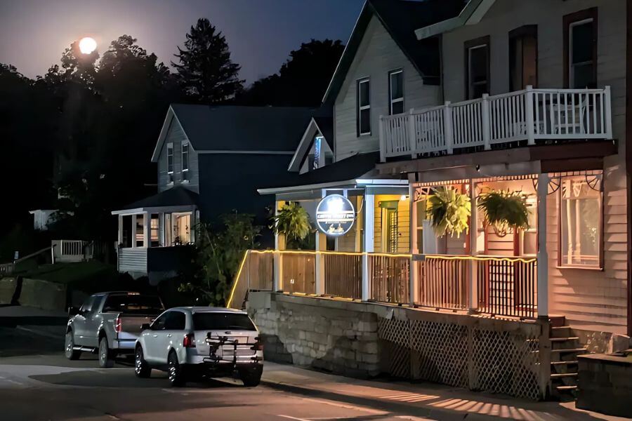 Coffee Street Inn in Lanesboro, Minnesota, illuminated at night with its glowing sign and porch lights, with a full moon rising above the nearby bluffs.