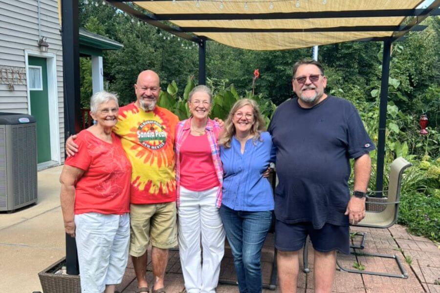 Group photo with owners Carrie and Rich Howe standing together on the right, smiling alongside other under a pergola.