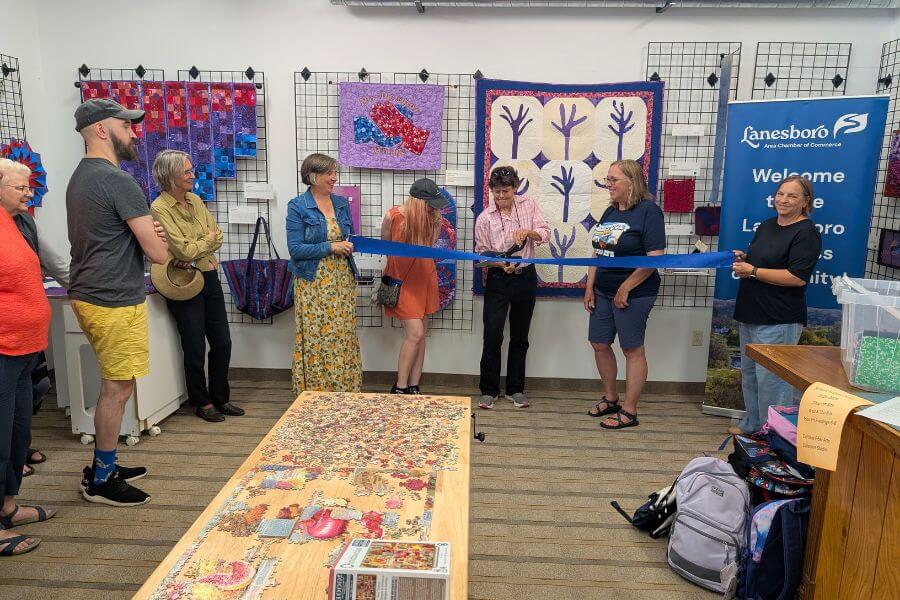 Founding members of the Driftless Fiber Arts Collective cut a blue ribbon during the opening celebration, surrounded by quilts and fiber art in the studio.