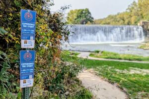 Talking Trail signs posted near the Lanesboro Dam, with the waterfall flowing in the background along the Root River.
