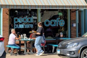 Server delivers plates of food to guests seated at outdoor picnic tables in front of Pedal Pushers Café in downtown Lanesboro, Minnesota.