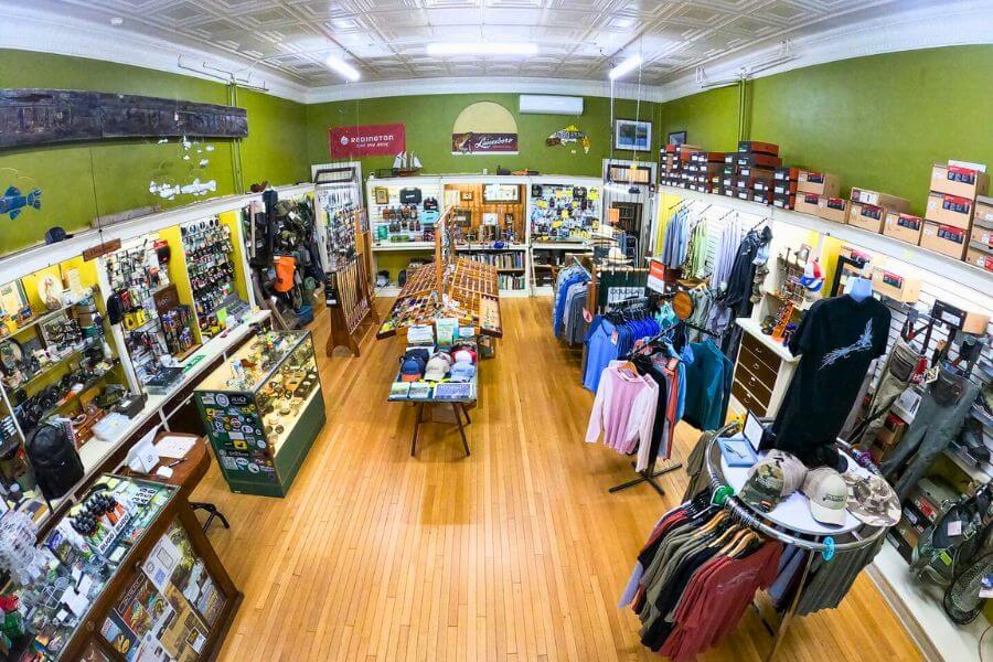 Interior view of Root River Rod Co. in Lanesboro, Minnesota, featuring displays of fly fishing gear, apparel, hats, and outdoor equipment arranged neatly inside the historic shop building.