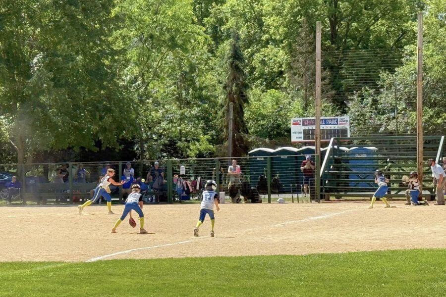 Kids playing softball on a sunny afternoon at the historic Whalan Ball Field, with spectators watching from the sidelines.