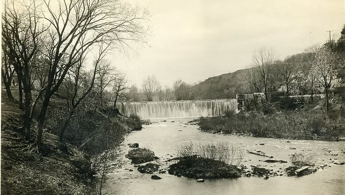 Historic photograph of the Lanesboro Stone Dam on the Root River in Minnesota, surrounded by bare trees and bluffs during the early settlement era.