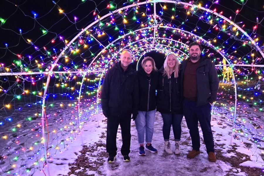 Four people stand beneath a glowing tunnel of colorful holiday lights at night in Lanesboro, Minnesota, surrounded by snow and festive cheer.