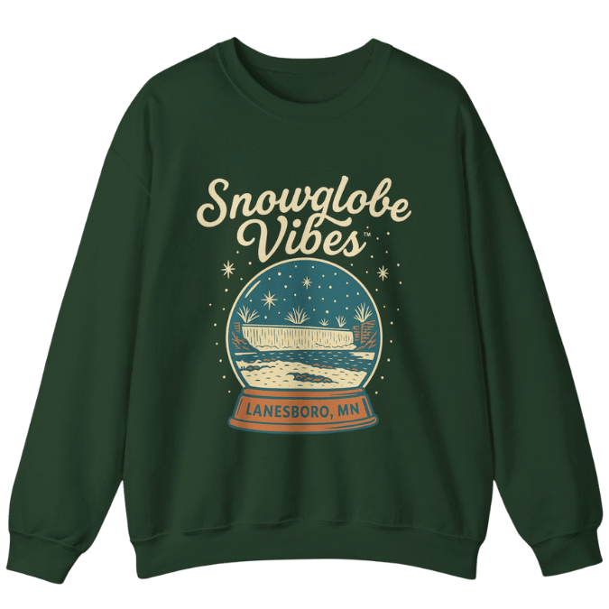 A dark green sweatshirt featuring a vintage-style illustration of the Lanesboro Dam inside a snowglobe, with the words “Snowglobe Vibes – Lanesboro, MN” printed above and below the design.