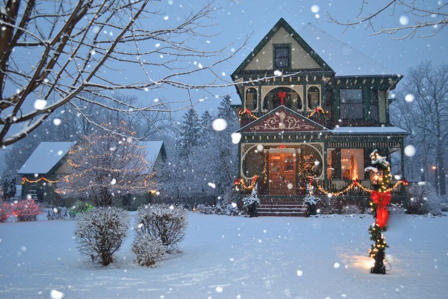 A Victorian-style home in Lanesboro decorated with Christmas lights and garlands during a snowy winter evening.