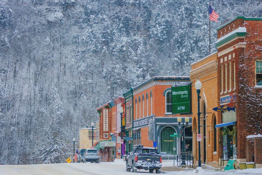 Downtown Lanesboro, Minnesota, lined with historic brick buildings and colorful storefronts beneath snow-covered bluffs on a peaceful winter day.
