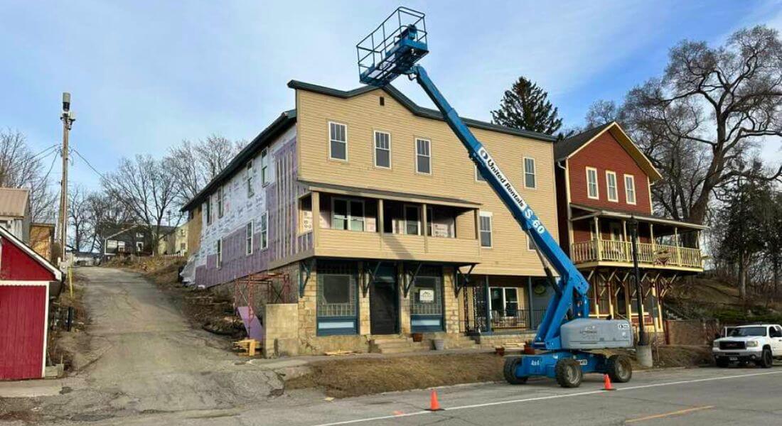 A blue boom lift reaches the roofline of a historic multi-story building in downtown Lanesboro during an exterior renovation project.