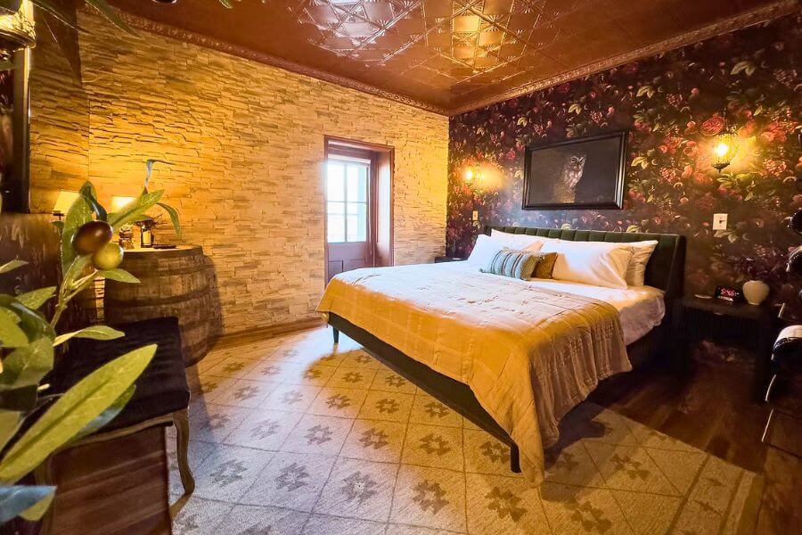 Cozy themed guest room at Hotel Lanesboro with a king bed, warm lighting, floral wallpaper, and stone accent wall in downtown Lanesboro, Minnesota.
