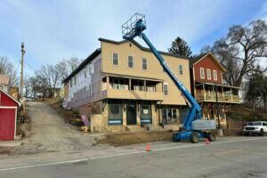 A blue boom lift reaches the roofline of a historic multi-story building in downtown Lanesboro during an exterior renovation project.
