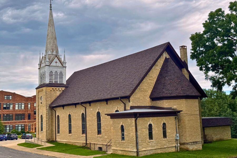A historic stone church with a newly completed dark shingle roof, showcasing detailed craftsmanship and preservation work in Lanesboro, Minnesota.