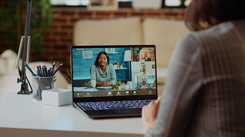 Remote employee talks with international multiethnic board of directors during videocall meeting from bright apartment. Teleworker in living room chats in teleconference call with business executives