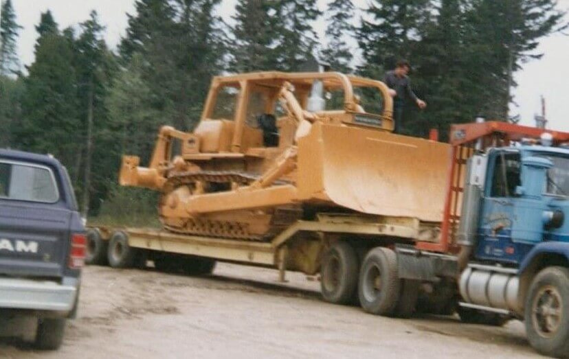 Pelletier logging truck hauling a bulldozer on a flatbed in Allagash Maine Northern Maine woods operation