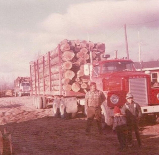 Pelletier family members standing beside a loaded red logging truck in Northern Maine early years of Pelletier Lumber