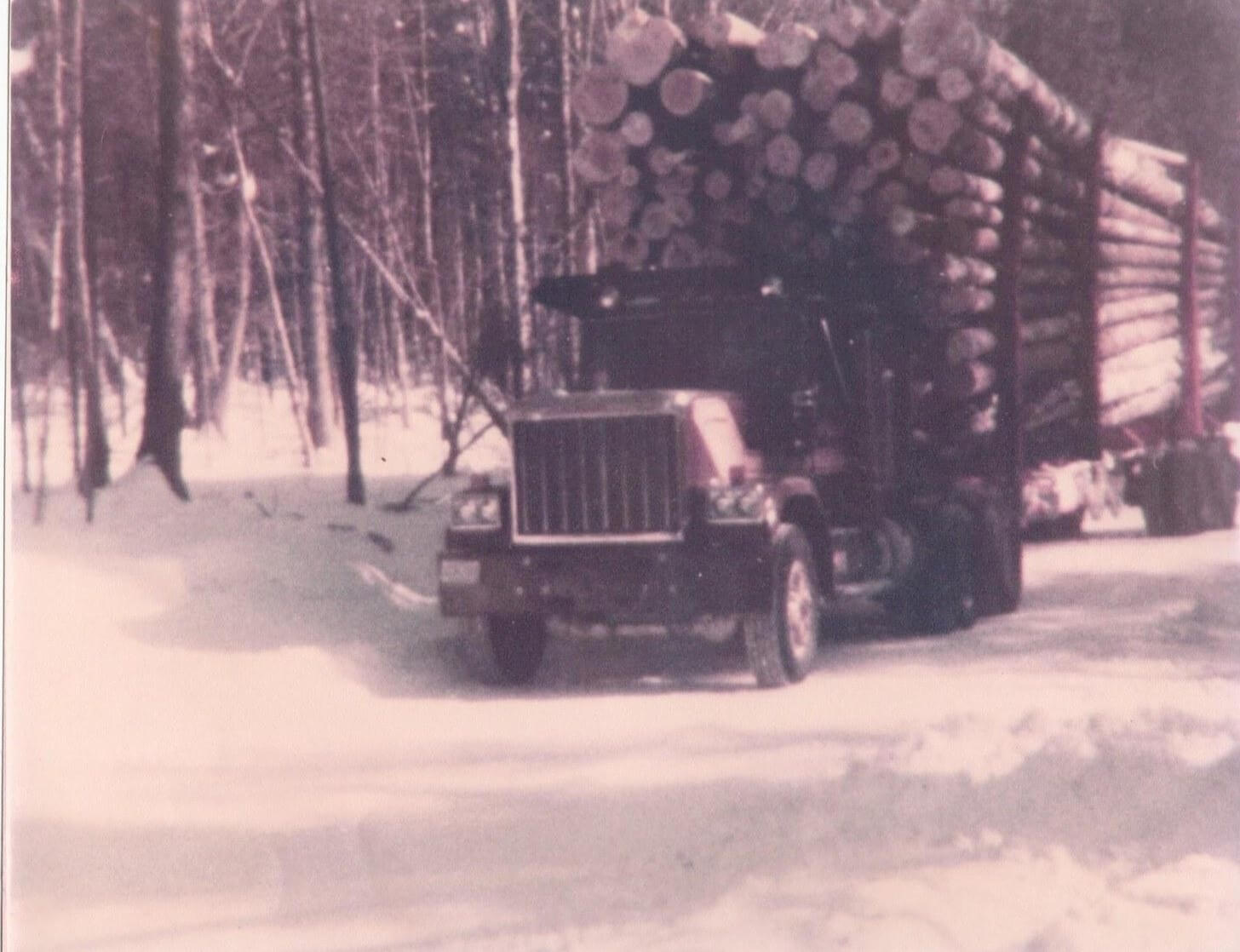 Pelletier logging truck loaded with timber driving through a snowy Northern Maine forest in winter