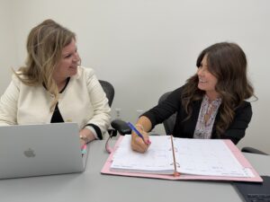 Two women seated at a table, collaborating on work together on a paper and on a laptop