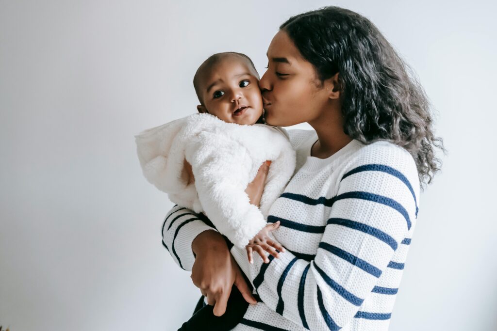 woman in a black and white striped shirt holding and kissing a smiling baby in a puffy white coat