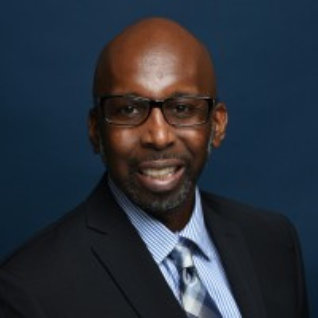 man smiling in suit and tie against a blue background