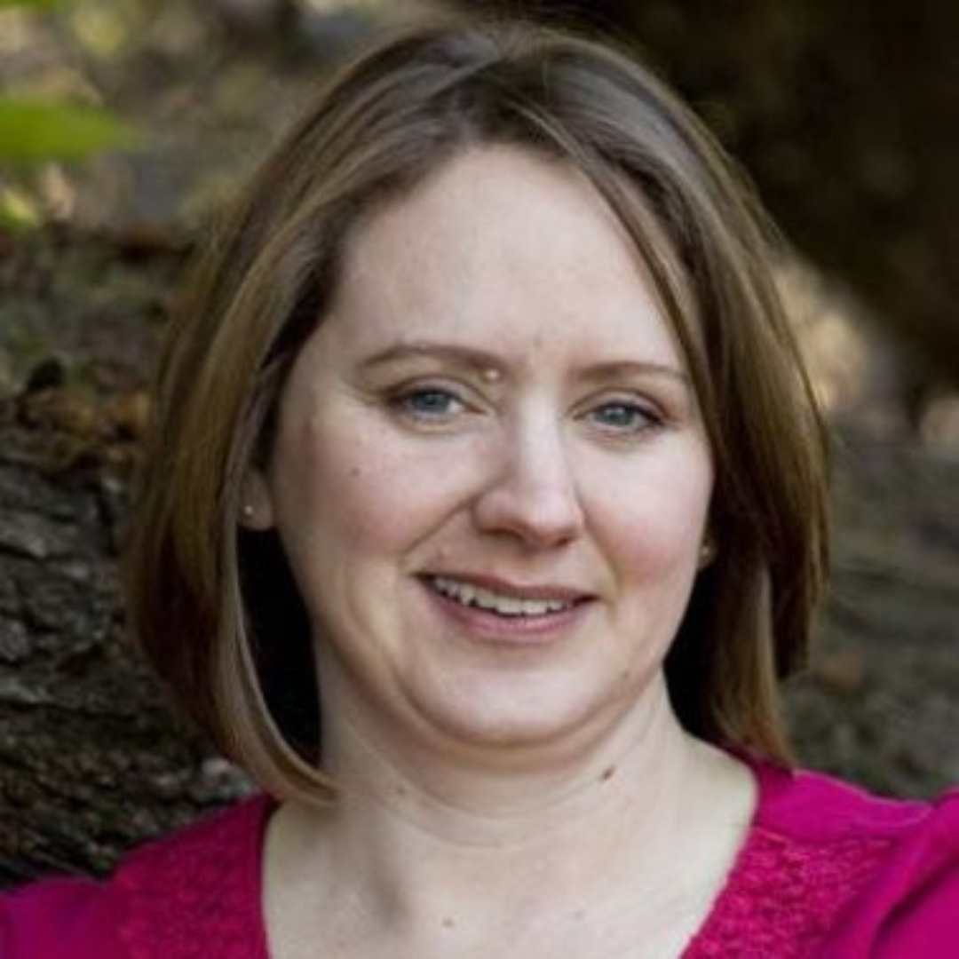 woman in pink shirt smiling with short hair against a tree
