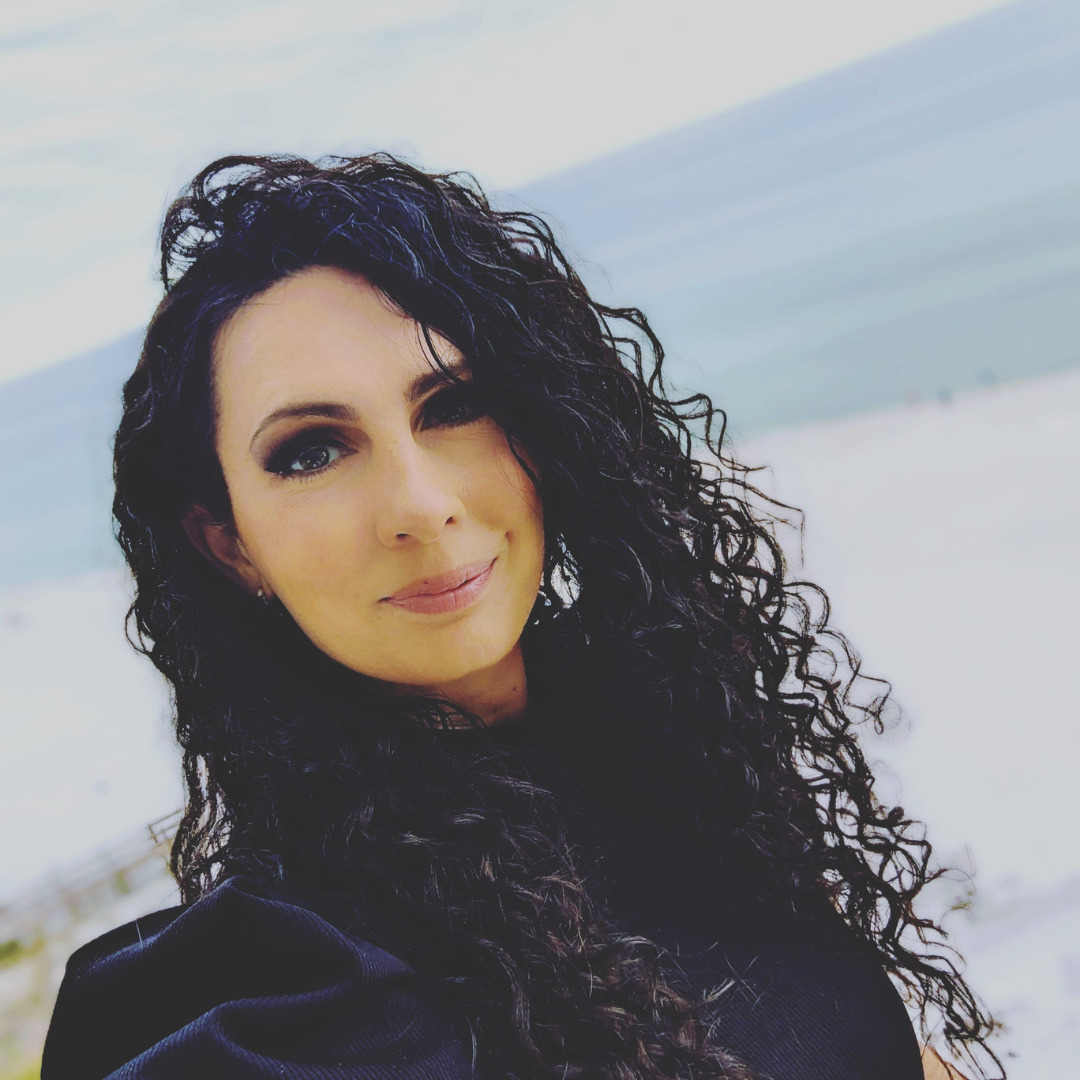 woman smiling with black curly hair with a beach in the background