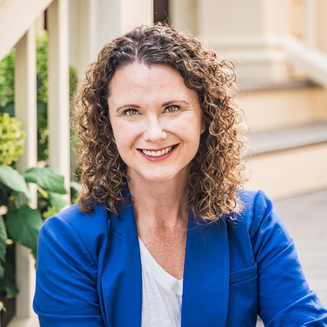 woman smiling in blue suit with brown curly hair on the steps of a house