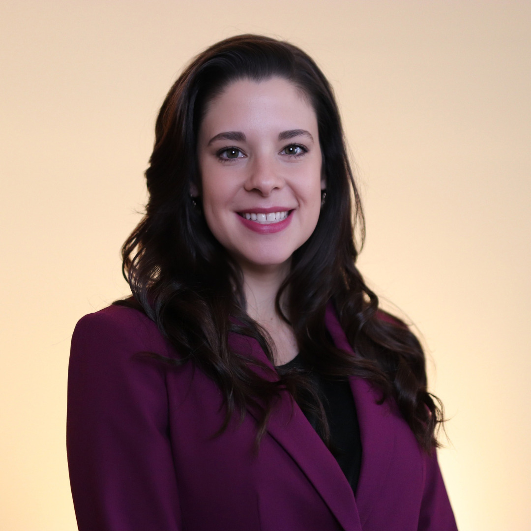 woman smiling in maroon suit and a black shirt with dark hair against a beige background