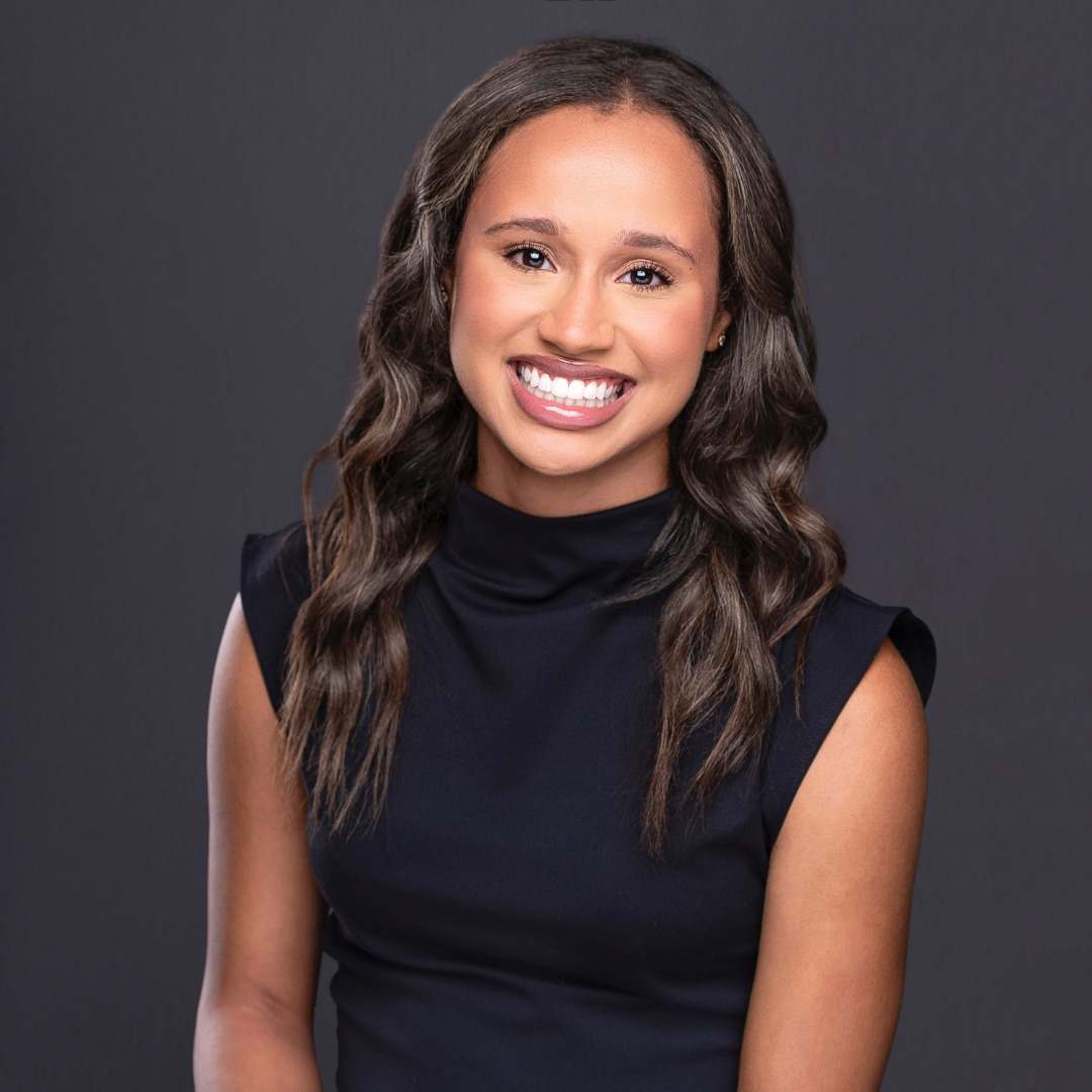 woman smiling with dark hair in a black top against a dark gray background