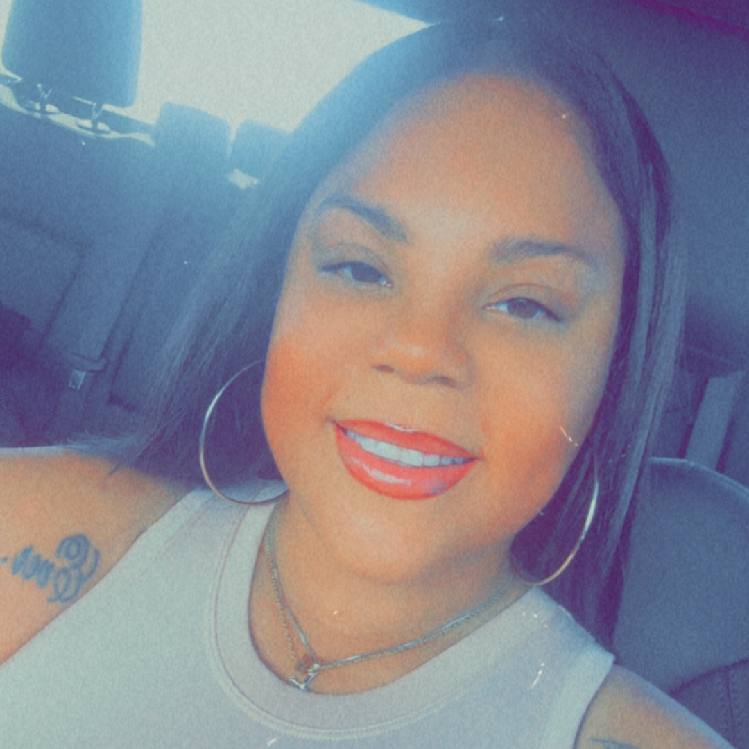 woman smiling in tanktop in a car with hoop earrings