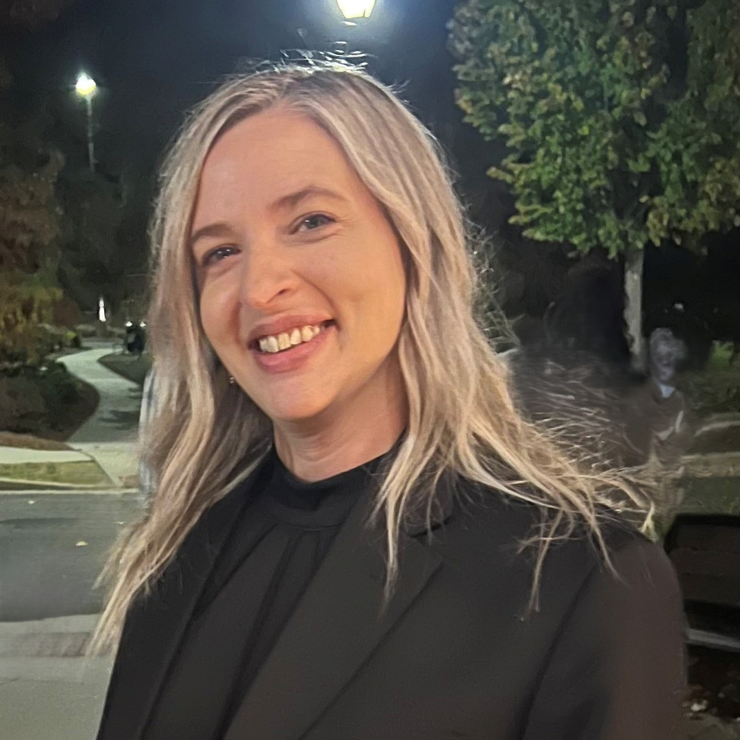 woman smiling in a black suit and blonde hair outside at nighttime