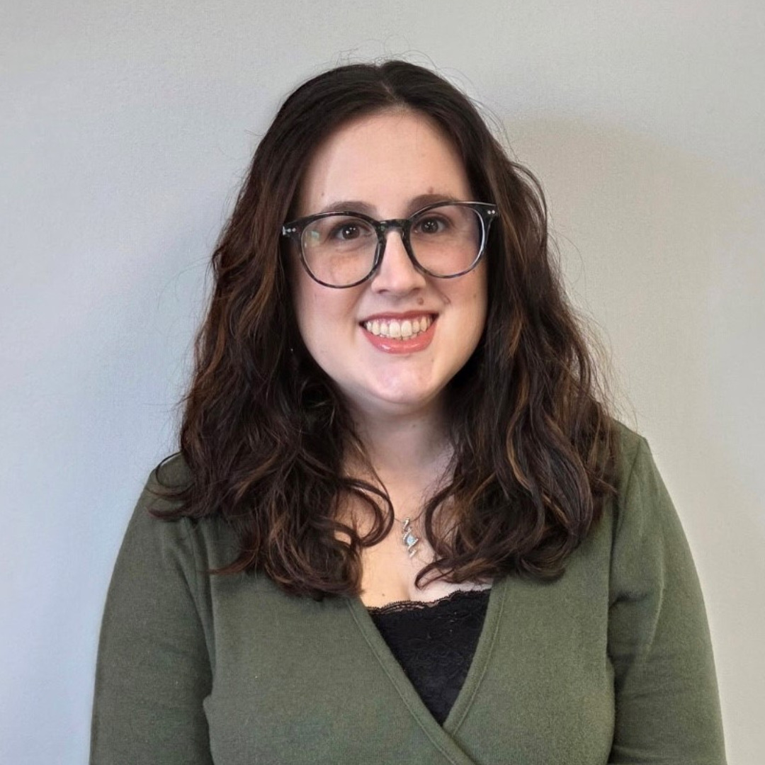 Savannah McDowell woman with glasses and brown hair smiling against a beige wall
