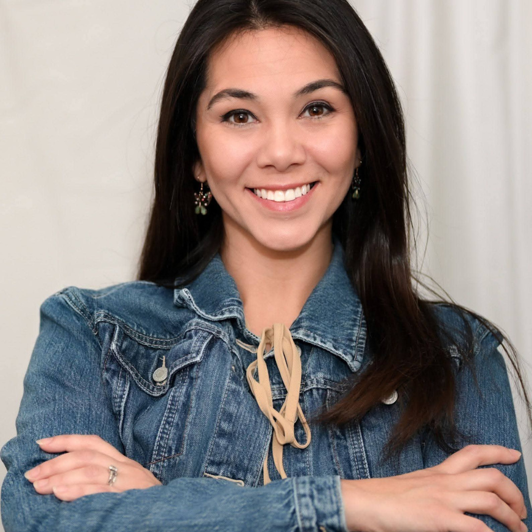 woman with black hair smiling with her arms crossed in a denim jacket
