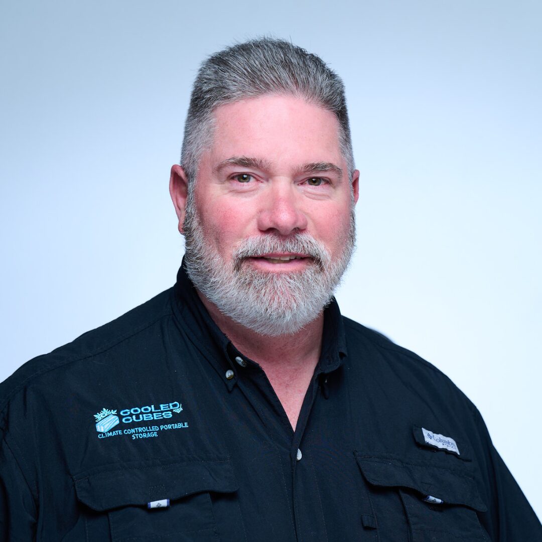 man in black button up shirt smiling at camera with light blue background