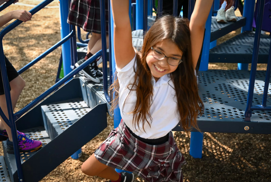 girl with brown hair and glasses hanging from playground equipment