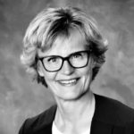 black and white photograph of female. Short light hair, glasses. dark jacket over light colored shirt