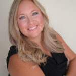 Beth coleman The image shows a professional headshot of a woman in her 30s or early 40s. She has long, wavy blonde hair that frames her face, bright blue eyes, and a warm, friendly smile. She’s wearing a simple black sleeveless top and accessorized with a stack of bracelets on her wrist. The background is neutral and softly lit, keeping the focus entirely on her approachable, confident expression.