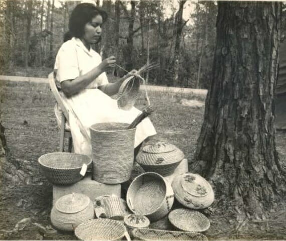 Ena Mae Sickey poses for a photo sewing a pine needle basket in front of a large collection of pine needle baskets, c. 1960s.
Images may not be reproduced or used in any way without the express written permission of the Coushatta Tribe of Louisiana Tribal Archives.