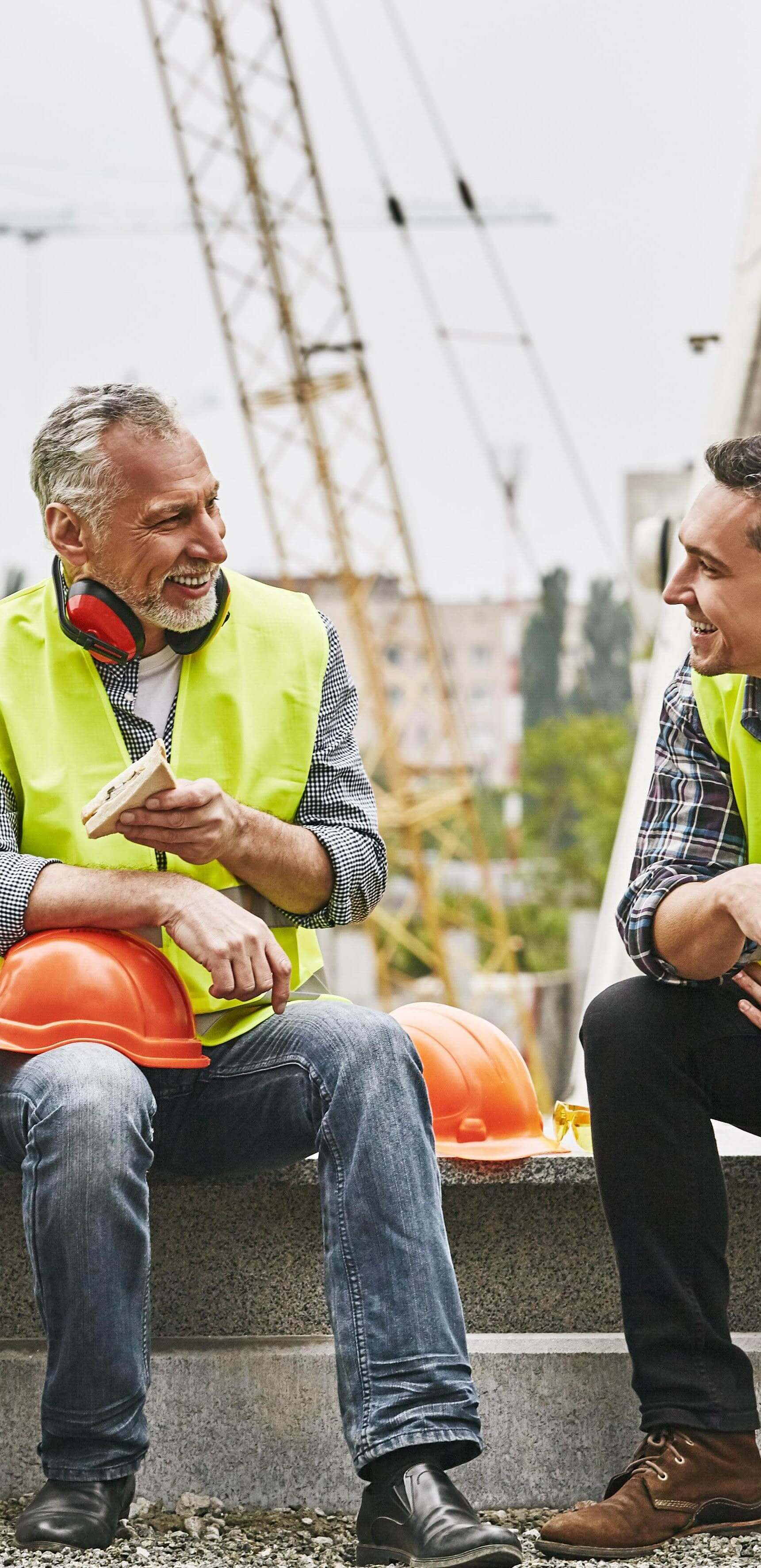 Time for a break. Group of builders in working uniform are eating sandwiches and talking while sitting on stone surface against construction site. Building concept. Lunch concept. Building concept