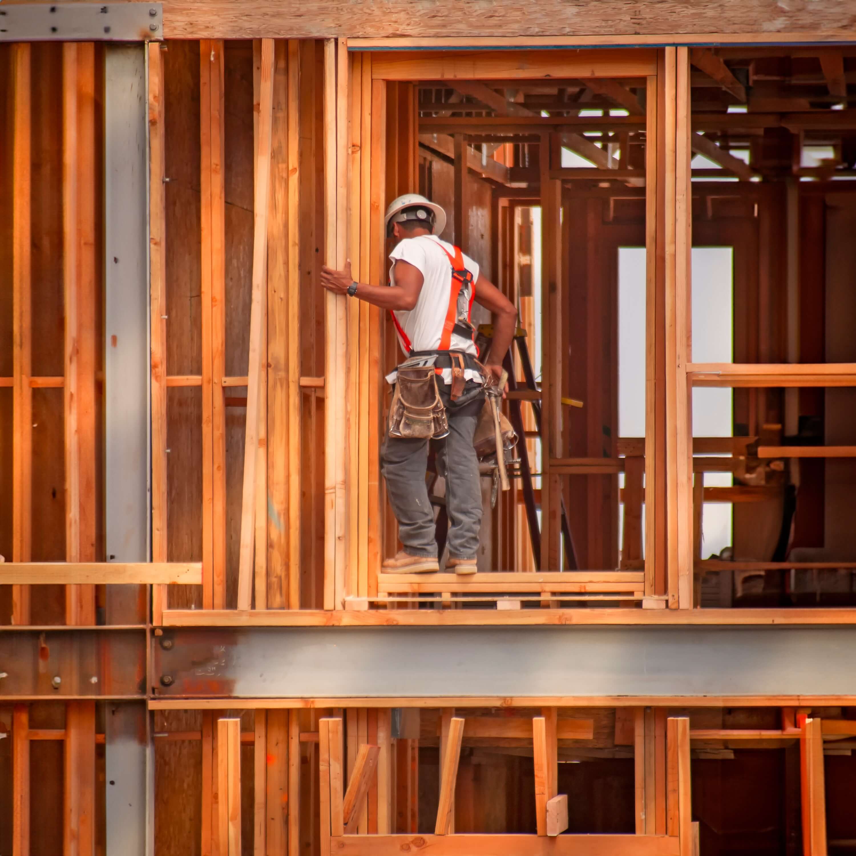 Vertical image of a construction worker wearing a tool belt standing in wood framing for a window.