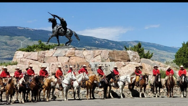 More than a dozen Outriders on horseback line up in front of the bronze monument known as "The Scout".
