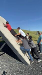 Group of 6 helping each other over an obstacle course wall.