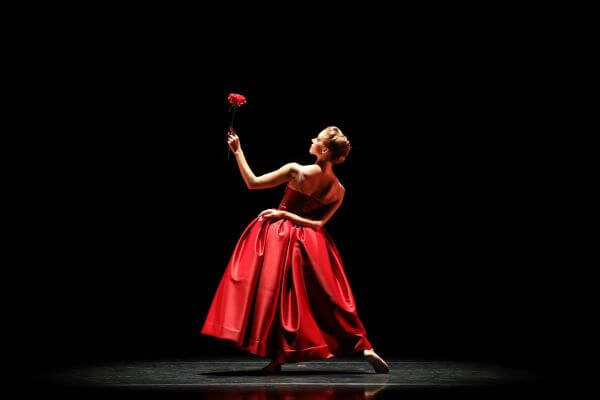 Photo of a ballerina in a red dress, holding a red rose.